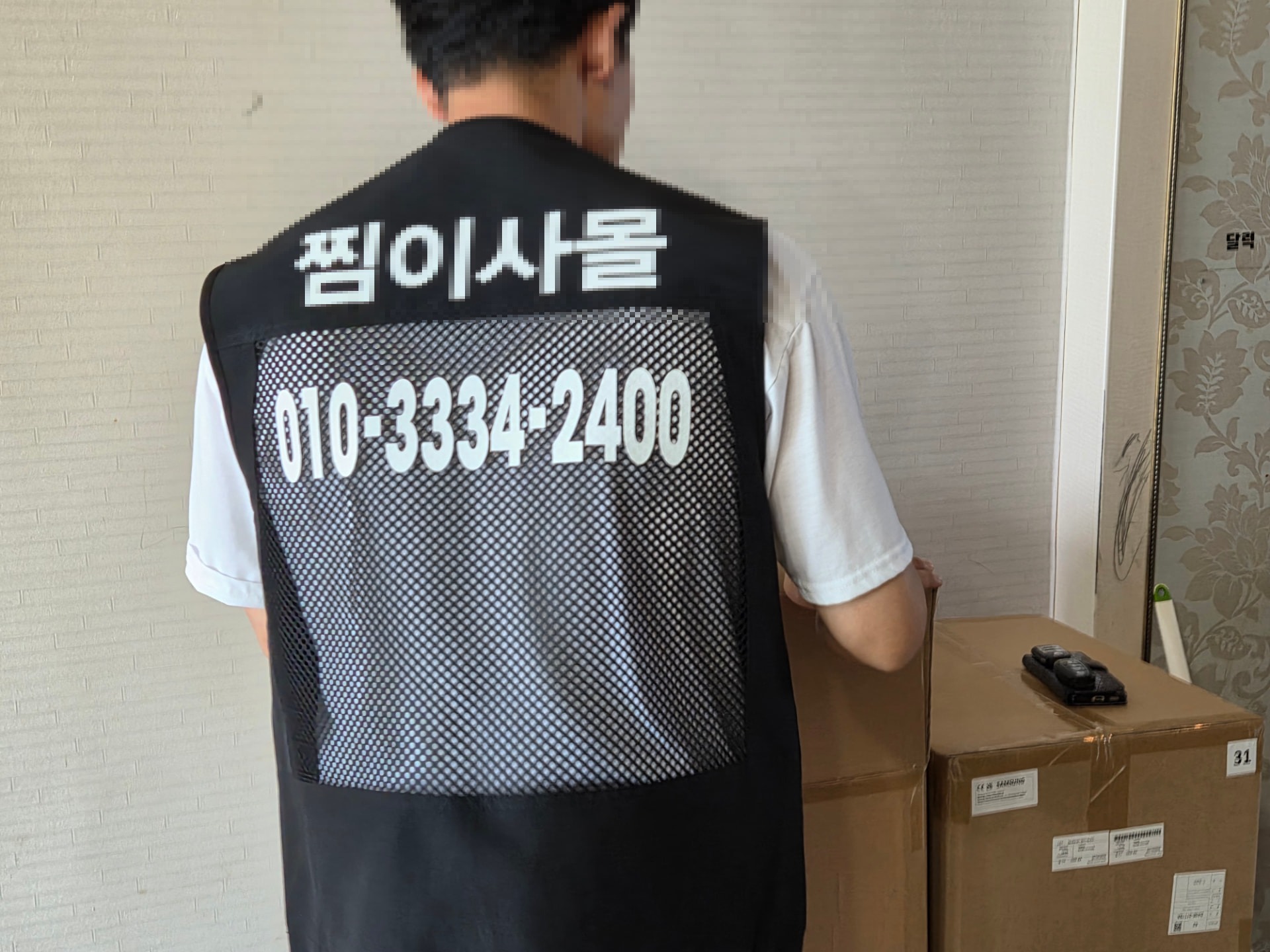 찜이사몰 조끼를 입은 작업자가 대형 가전 박스를 확인하는 모습