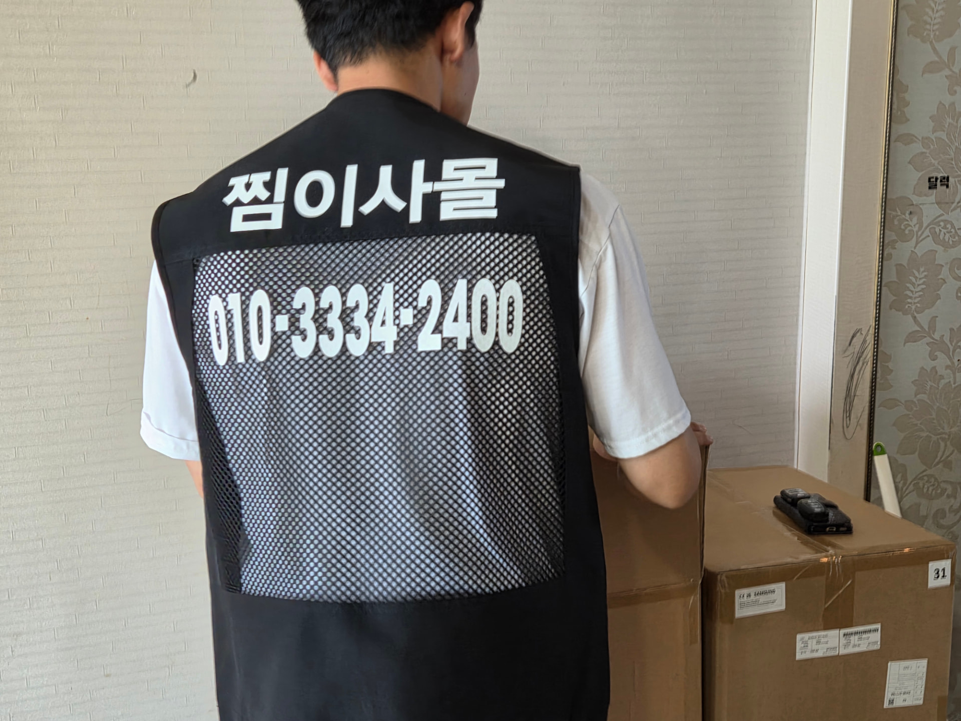 찜이사몰 조끼를 입은 작업자가 대형 가전 박스를 확인하는 모습